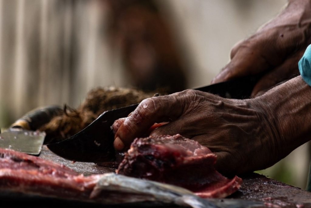 Hands slicing fish with knife.