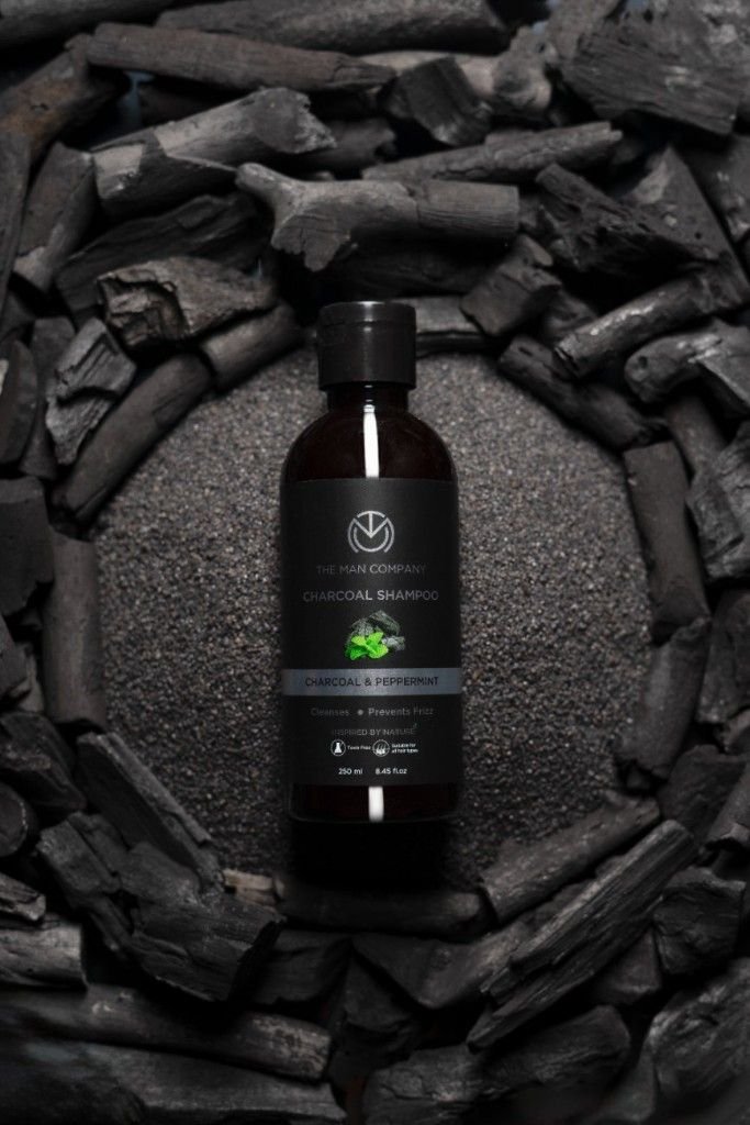 A shampoo bottle on black sand surrounded with charcoal.