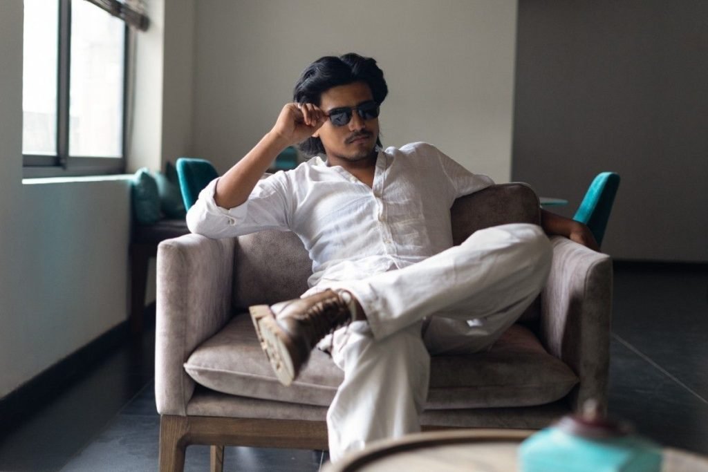 A male model is sitting on a sofa.