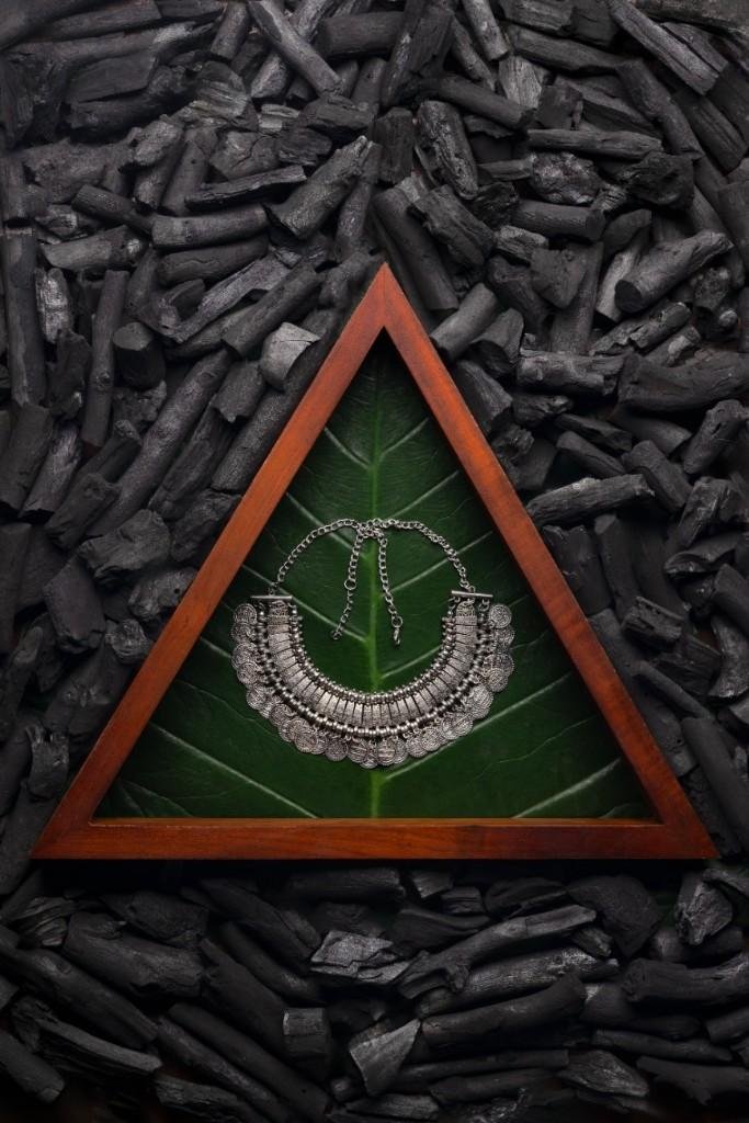 A silver necklace on a leaf surrounded by charcoal.