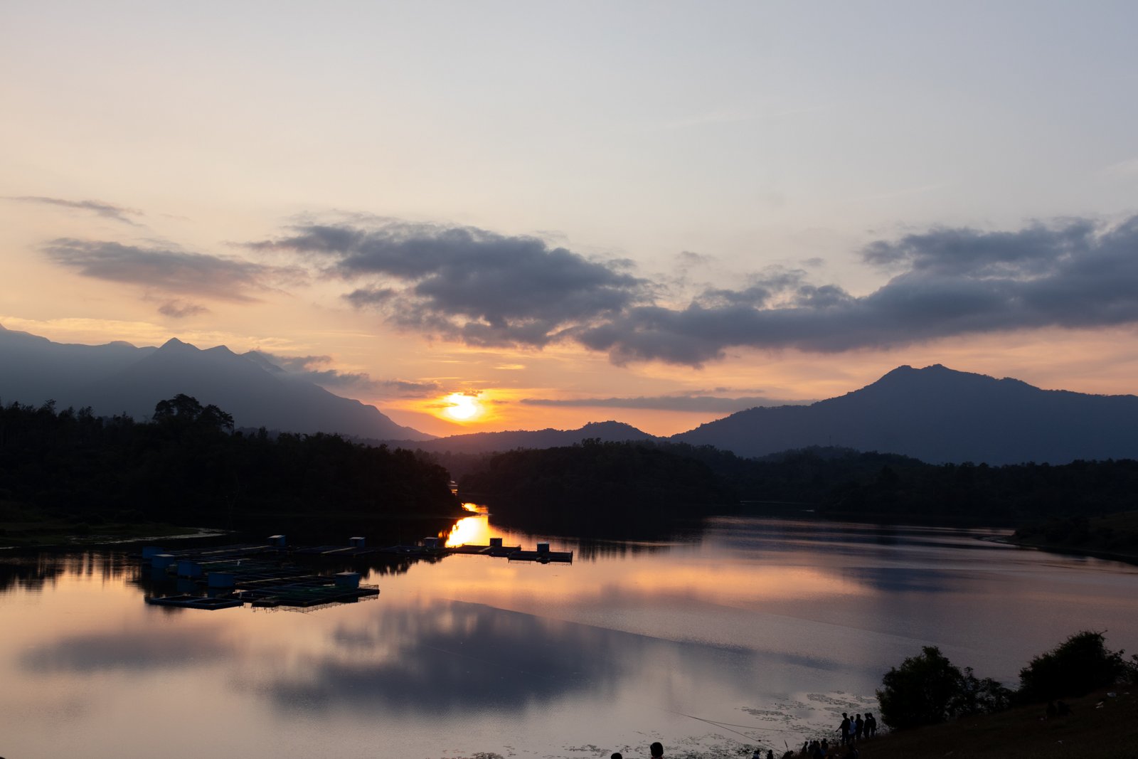 Calm waters and mountains with sun setting in background.