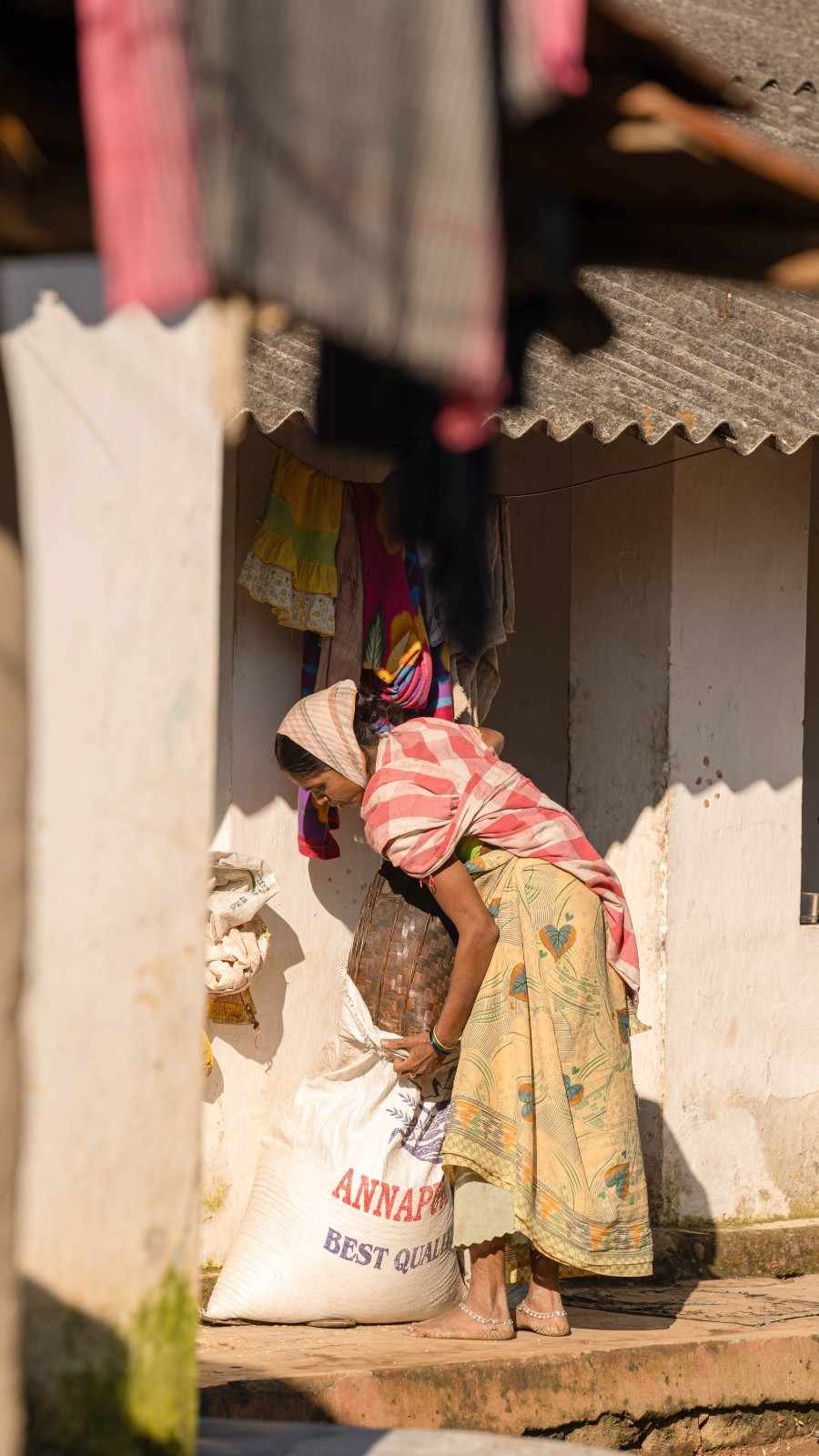 a lady is carrying grains bag out of her home
