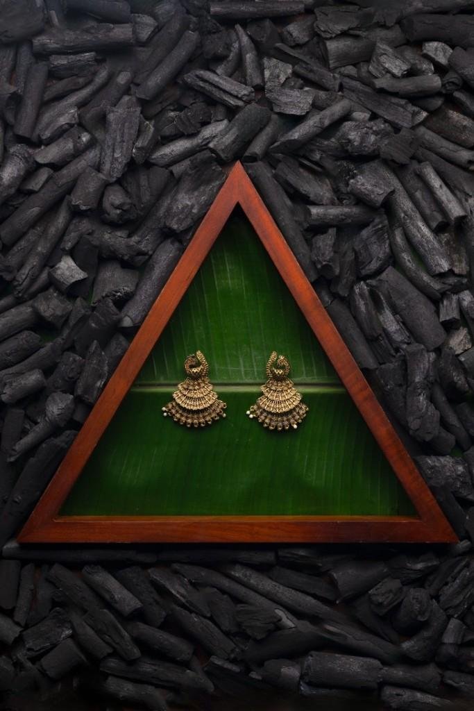 A golden earring on a leaf surrounded by charcoal.