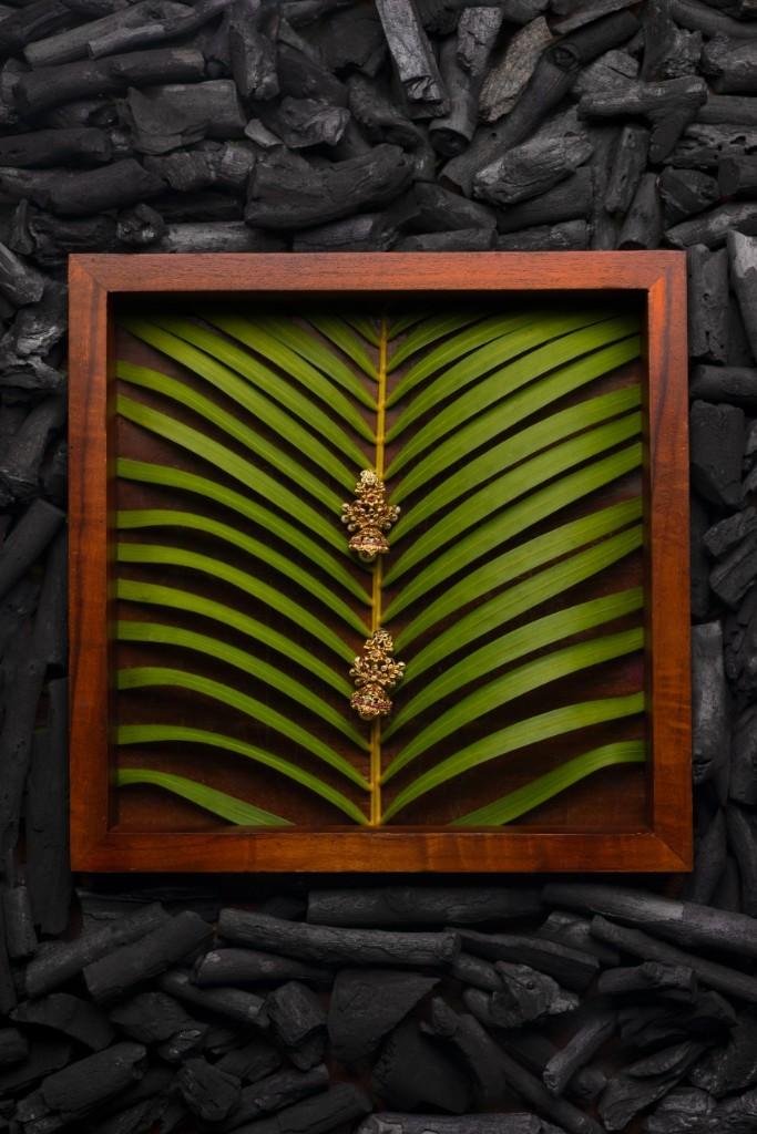 A golden earring on a leaf surrounded by charcoal.