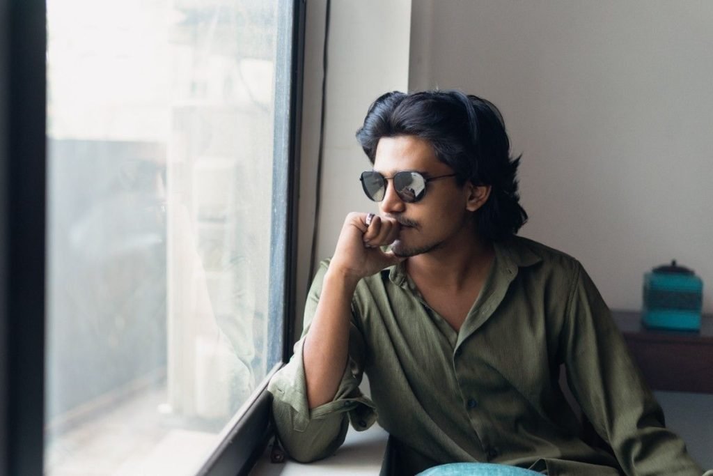 A male model is sitting at the window side.