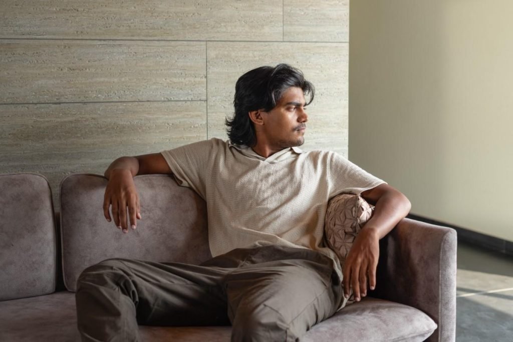 A male model is sitting on a sofa.