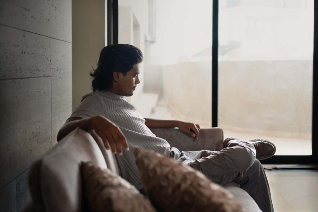 A male model is sitting on a sofa.